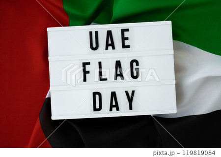 Lightbox with text UAE FLAG DAY on United Arab Emirates waving flag made from silk material. Independence Commemoration Day Muslim Public holiday celebration background. The National Flag of UAE 119819084