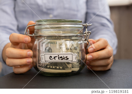 Female hands holding Glass jar full of American currency dollars cash banknote with text CRISIS. Preparation saving money. Moderate consumption and economy Female hands holding Glass jar full of American currency dollars cash banknote with text CRISIS. Preparation saving money. Moderate consumption and economy 119819181