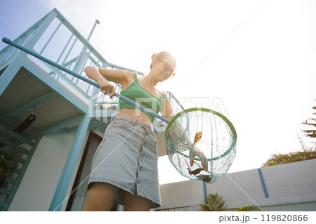 A young woman clean leaves out of a pool A young woman clean leaves out of a pool 119820866