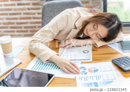 Tired young businesswoman lays her head down on her arm sleeping at her office desk Tired young businesswoman lays her head down on her arm sleeping at her office desk 119821345