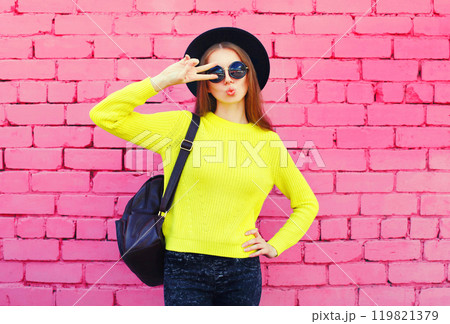 portrait stylish young woman in black hat, yellow knitted sweater on colorful pink background 119821379