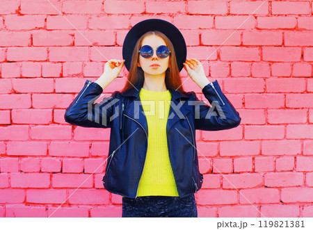 Fashion young woman wearing a black hat, jacket on colorful pink bricks background 119821381