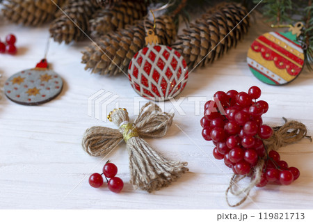DIY decorations for Christmas. Xmas card. Christmas composition with Ukrainian doll-motanka, wooden balls, guelder rose, cones and fir branches. New Year eco-conscious handmade toys. Happy holidays. DIY decorations for Christmas. Xmas card. Christmas composition with Ukrainian doll-motanka, wooden balls, guelder rose, cones and fir branches. New Year eco-conscious handmade toys. Happy holidays. 119821713