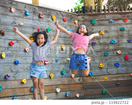 Children play outdoors on a wooden playground in a park. Happy girl playing on wooden climbing wall in playground during summer. Children play outdoors on a wooden playground in a park. Happy girl playing on wooden climbing wall in playground during summer. 119822722