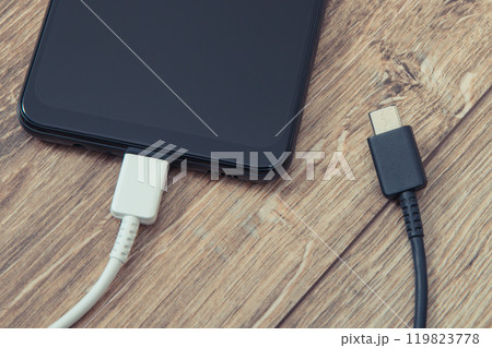 Black smartphone with charger cables on wooden background. Telephone charging concept Black smartphone with charger cables on wooden background. Telephone charging concept 119823778