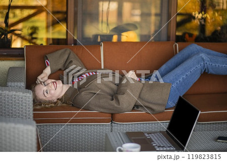 Balance productivity with relaxation to enhance creativity and performance. freelance woman lies on sofa outdoors, laptop 119823815