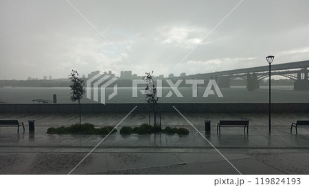 Cityscape with bridge over river in rain shower with bench and lamp post in foreground Cityscape with bridge over river in rain shower with bench and lamp post in foreground 119824193