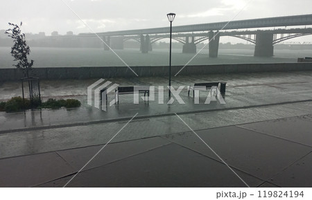Cityscape with bridge over river in rain shower with bench and lamp post in foreground Cityscape with bridge over river in rain shower with bench and lamp post in foreground 119824194
