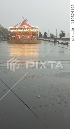 Lonely Deserted Carousel In The Rain With Bright Lights And A Glimmering Reflection On The Ground 119824196