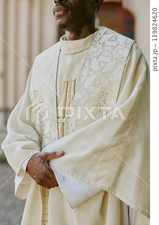 Vertical shot of unrecognizable priest dressed in golden white robe crossed his hands while standing outside 119824620