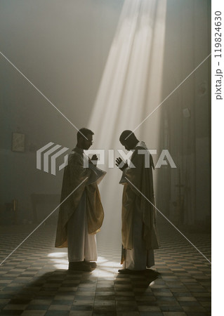 Vertical shot of priests in white robes clasped their hands beneath golden sunrays 119824630