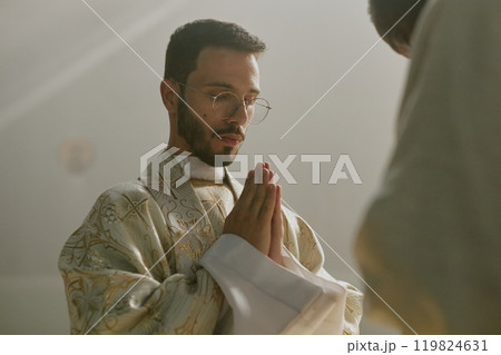 Low angle shot of Caucasian priest in white robe praying with closed eyes 119824631