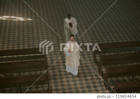 High angle shot of biracial priests in golden white robes with candle and Bible in hands going through nave 119824654