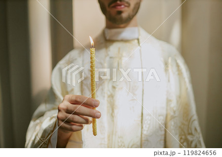 Medium close up of unrecognizable priests hand holding thin candle during church service 119824656