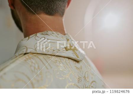 Medium close up of unrecognizable priest wearing white robe with golden embroidered cross and patterns 119824676
