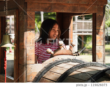 Children play outdoors on a wooden playground in a park. Happy girl playing with wooden train in playground during summer. Children play outdoors on a wooden playground in a park. Happy girl playing with wooden train in playground during summer. 119826073