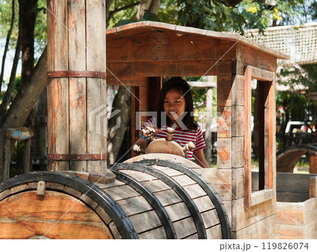 Children play outdoors on a wooden playground in a park. Happy girl playing with wooden train in playground during summer. 119826074