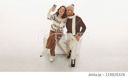 Happy, smiling young couple, man and woman dressed in cozy winter clothes taking selfie before ice skating isolated on white background 119826329