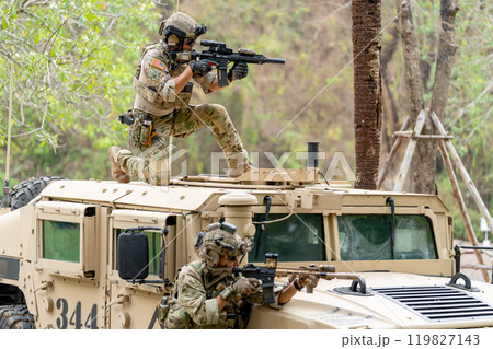 Two militaries or soldiers stay near humvee car with on on roof and the other one in area of car hood also point gun to right side during outdoor practice. 119827143
