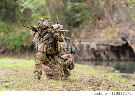 Two militaries or soldiers stay in battlefield near the river with sit down and point gun in different direction during outdoor practice. 119827179
