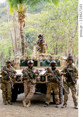 Vertical image of group of militaries or soldiers stay in front of humvee car and one stay on car roof also look at camera during outdoor practice. Vertical image of group of militaries or soldiers stay in front of humvee car and one stay on car roof also look at camera during outdoor practice. 119827183