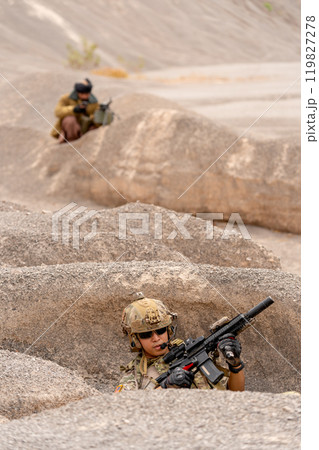 Vertical image military or soilder man hold gun and sit in the pit or slope in front of the terrorist who stay in back of battlefield in area near mountain. 119827278