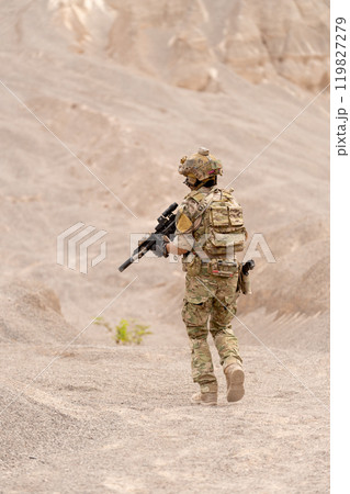 Vertical image back of military or soldier with hold gun and walk in battlefield near the mountain during outdoor practice. 119827279
