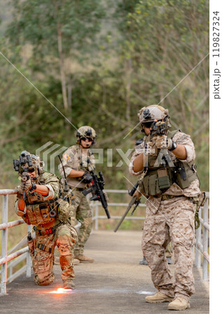 Vertical image military or soldier team with battle suit stay on the bridge near flare firework in position for battle and point gun different direction during outdoor practice. 119827324