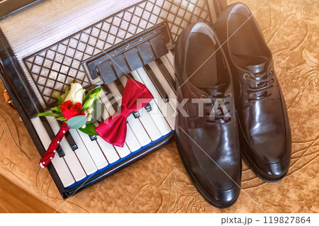 Elegant Groom's Accessories Arranged on a Vintage Piano Near a Wedding Setting. 119827864