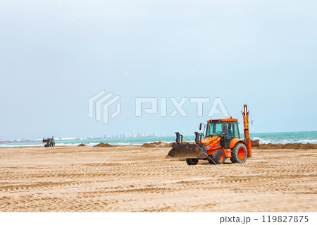 Heavy Machinery Clearing Sand and Seaweed From a Beach on a Sunny Day Near the Coastline 119827875