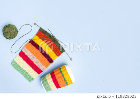 Cup for takeaway coffee with knitted autumn striped cover and knitted wool with knitting needles on blue background. Concept of takeaway coffee, walking, energetic life, hobbies needlework 119828025