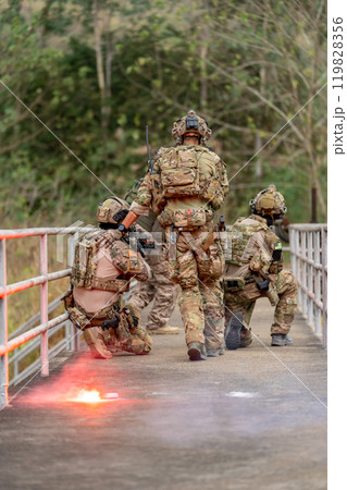 Vertical image back of of military or soldier team with battle suit stay on the bridge near flare firework in position for battle and point gun different direction during outdoor practice. Vertical image back of of military or soldier team with battle suit stay on the bridge near flare firework in position for battle and point gun different direction during outdoor practice. 119828356