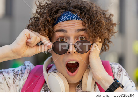 Happy man taking off sunglasses looking surprised at camera with big open eyes, shocked by victory 119829294