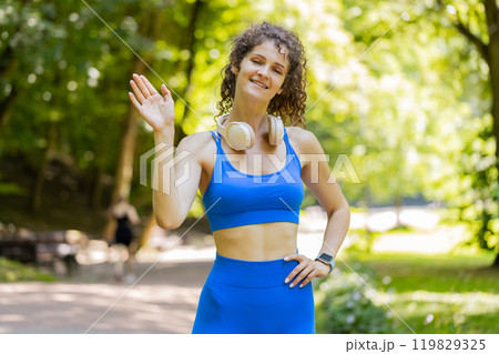 Athletic fit slim runner woman waving hi hello with hand greeting with hospitable friendly smile 119829325