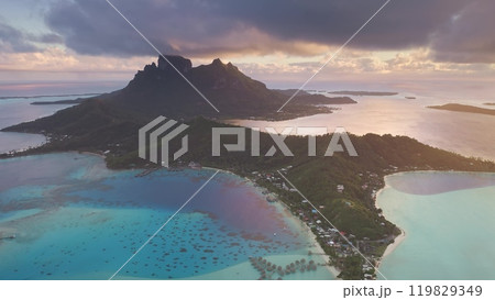 Amazing tropical island sunset. Drone fly over Bora Bora, mount otemanu and turquoise lagoon glowing under dramatic colorful clouds sky. Remote wild nature paradise, exotic summer travel background Amazing tropical island sunset. Drone fly over Bora Bora, mount otemanu and turquoise lagoon glowing under dramatic colorful clouds sky. Remote wild nature paradise, exotic summer travel background 119829349