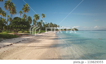 Paradise island beach with palm trees and turquoise blue water gently laps white sand shore in sunny day. Tourists enjoying tropical paradise. Remote wild nature, exotic summer travel background 119829355
