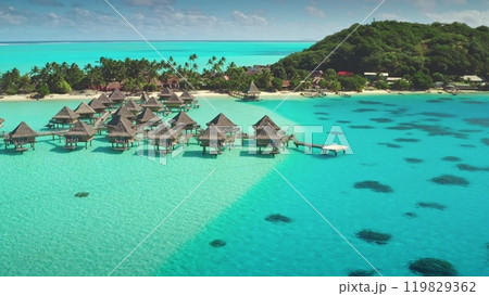 Luxury overwater bungalows in turquoise crystal clear lagoon with tropical island sand beach in background. Aerial drone view of perfect exotic summer travel luxury vacation. Wild nature background 119829362