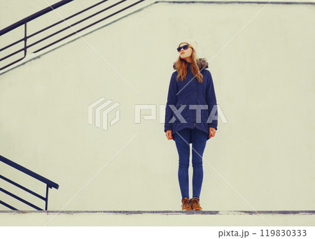 Fashion pretty blonde woman wearing jacket and hat posing in winter city over white wall background 119830333