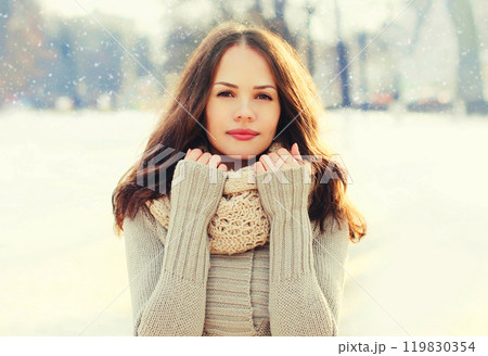 Portrait pretty young woman wearing a knitted sweater and scarf in winter day over snowflakes 119830354