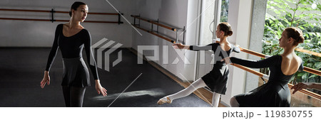 Website header shot female choreographer striking elegant pose teaching young girls ballet moves while children practicing at barre in sunlit dance studio Website header shot female choreographer striking elegant pose teaching young girls ballet moves while children practicing at barre in sunlit dance studio 119830755