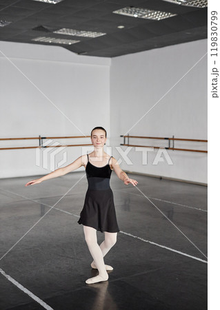Vertical shot of smiling teenage girl wearing black dress for dancing getting ready to perform series of pirouettes while practicing ballet moves in dance studio with no people, copy space Vertical shot of smiling teenage girl wearing black dress for dancing getting ready to perform series of pirouettes while practicing ballet moves in dance studio with no people, copy space 119830799