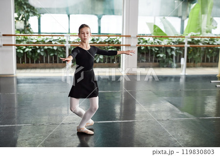 Full length shot of concentrated young girl wearing black dress for dancing getting ready to perform series of pirouettes while practicing ballet moves in dance studio with green plants, copy space Full length shot of concentrated young girl wearing black dress for dancing getting ready to perform series of pirouettes while practicing ballet moves in dance studio with green plants, copy space 119830803