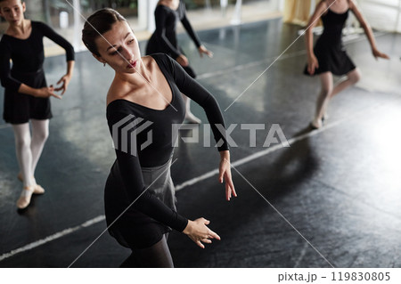 Side view of female dance teacher in black leotard gracefully moving practicing ballet positions while teaching little kids in studio, copy space Side view of female dance teacher in black leotard gracefully moving practicing ballet positions while teaching little kids in studio, copy space 119830805
