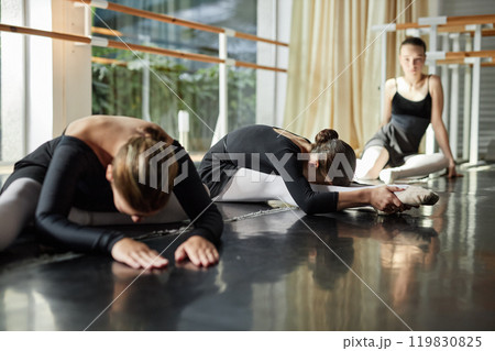 Side view of little female ballet dancer stretching muscles bending over legs while warming up on studio floor preparing for group class, copy space Side view of little female ballet dancer stretching muscles bending over legs while warming up on studio floor preparing for group class, copy space 119830825