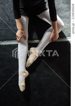 Vertical shot of unrecognizable female dancer wearing ballet slippers resting after class while sitting on floor in dance studio 119830826