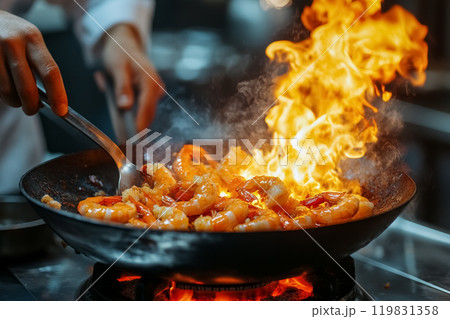Chef hands cooking dish stir fry shrimp with flame in frying pan on kitchen stove in restaurant, professional seafood preparation 119831358