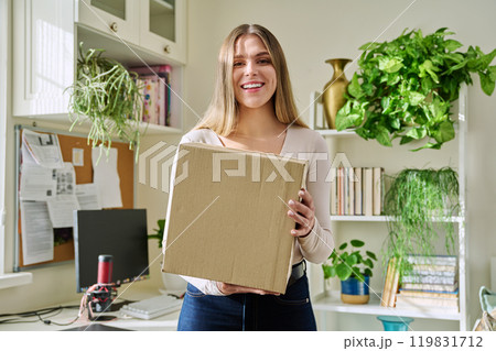 Young woman at home unpacks cardboard box with online purchases 119831712