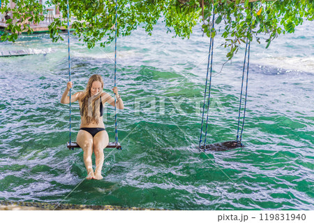 Beautiful female tourist relaxing on a swing in Laguna Bacalar in Mexico during kayak trip. Female tourist swinging over Lake Bacalar with feet in the water. Quintana Roo, Mexico travel, relaxation 119831940
