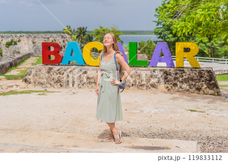 Female tourist posing in front of the colorful BACALAR sign with vibrant letters, trees, and Bacalar Lake in the background. Mexican travel and adventure concept Female tourist posing in front of the colorful BACALAR sign with vibrant letters, trees, and Bacalar Lake in the background. Mexican travel and adventure concept 119833112