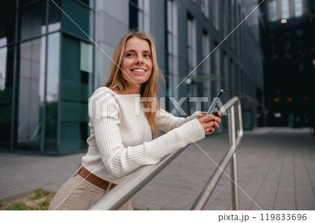 A Cheerful Woman with a Smartphone Captivatingly Posed in a Vibrant Urban Setting A Cheerful Woman with a Smartphone Captivatingly Posed in a Vibrant Urban Setting 119833696